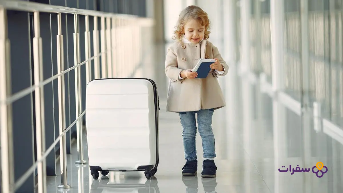 iraq travel requirements guide 4 طفلة صغيرة تقف مبتسمة بجانب حقيبة سفر صغيرة استعداداً للرحلة.